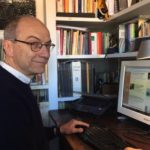 Il giornalista ambientale Antonio Cianciullo seduto alla sua scrivania, con il computer davanti e la libreria sullo sfondo